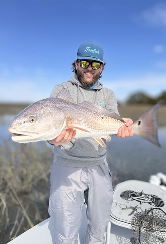 Man in Toadfish gear holding a big redfish in the saltwater marsh