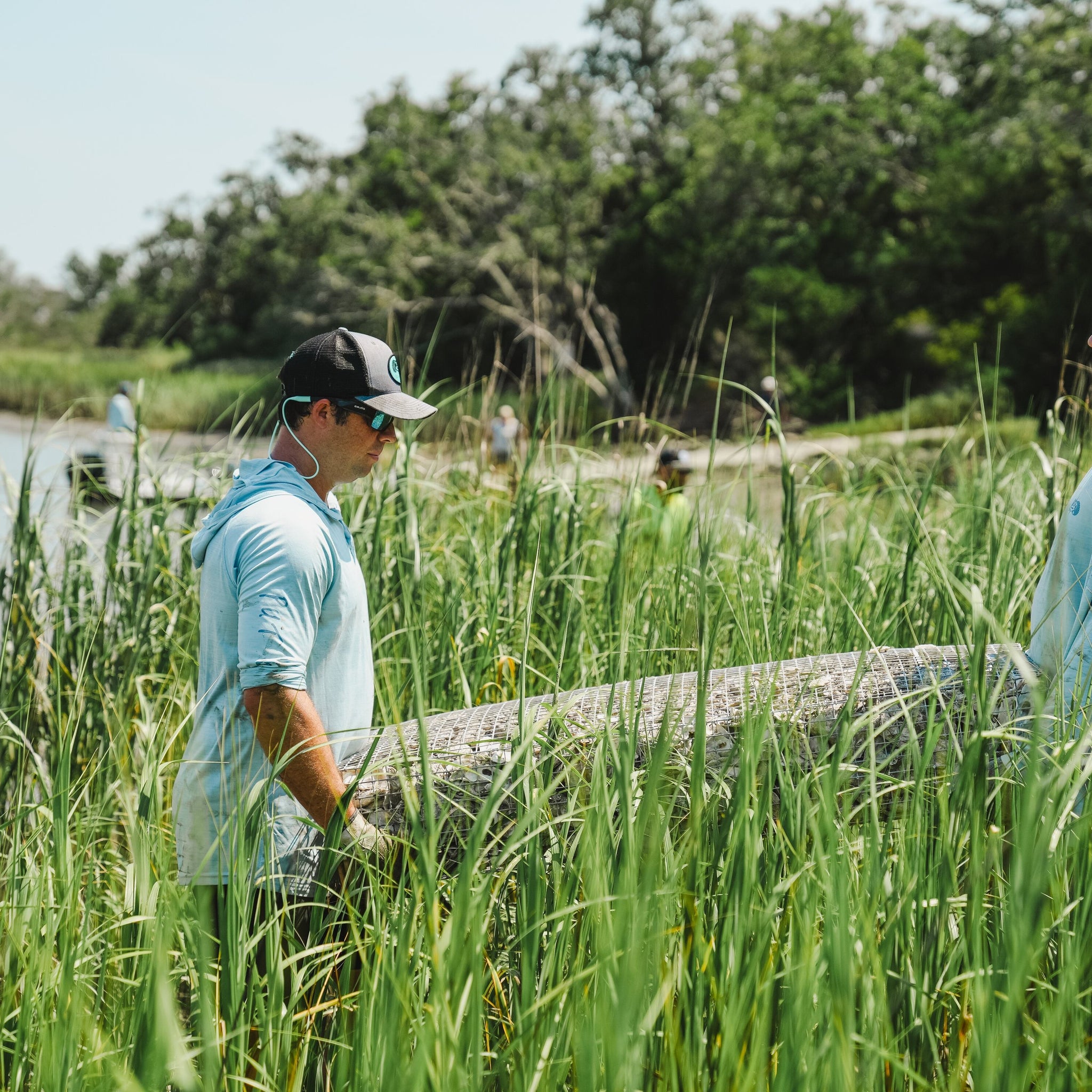 two men wearing toadfish gear are seen carrying an MWR through the marsh grass on their way to plant it in the pluff mud