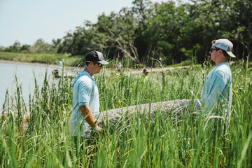 two men wearing toadfish gear are seen carrying an MWR through the marsh grass on their way to plant it in the pluff mud